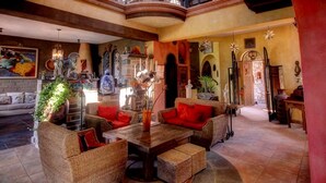 A spacious living room with wicker furniture, a fireplace, and various decorative items. - Hotel Casa Angelitos (San Miguel de Allende)