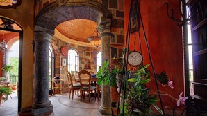 An interior with stone columns, a dining area with wooden chairs, and potted plants. - Hotel Casa Angelitos (San Miguel de Allende)