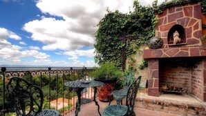 An outdoor patio with wrought iron furniture, a stone fireplace, and a view of the landscape. - Hotel Casa Angelitos (San Miguel de Allende)