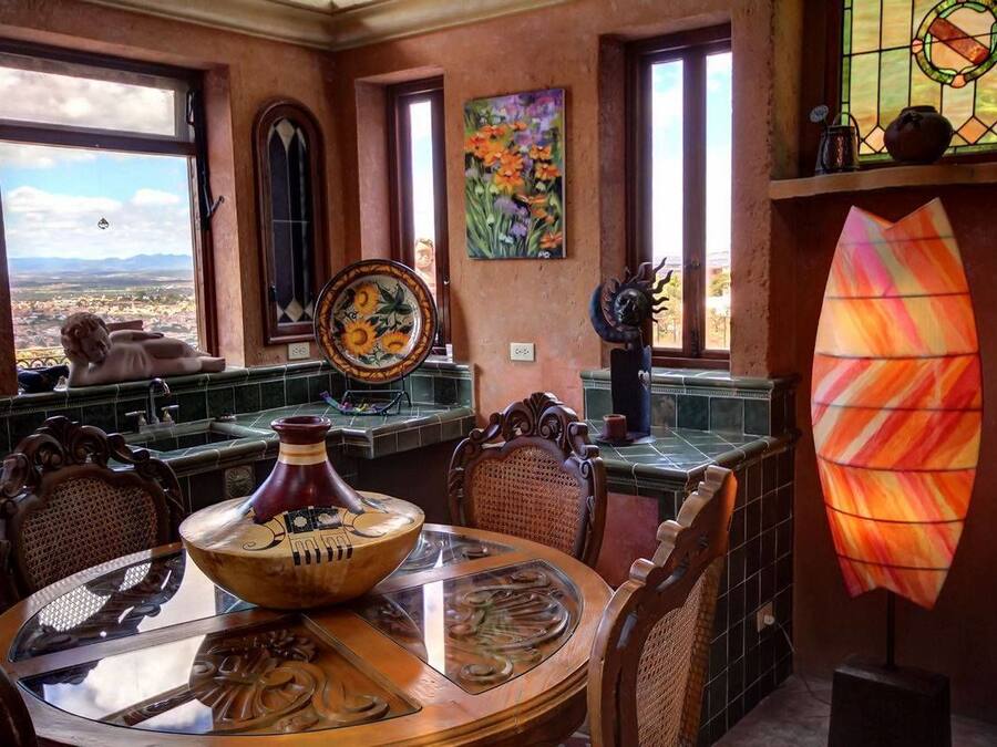 A dining area with a view, featuring a table with a bowl, chairs, and a stained glass window.