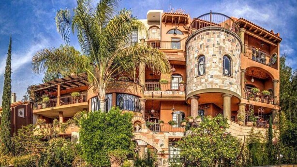 A multi-story building with a curved tower, balconies, and lush greenery. - Hotel Casa Angelitos (San Miguel de Allende)