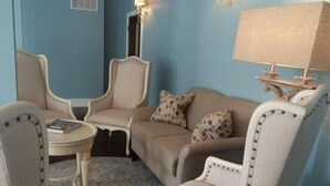 A room with a blue wall, a beige sofa, two armchairs, a small round table, and a lamp. - The Inn at Spring House (Block Island)