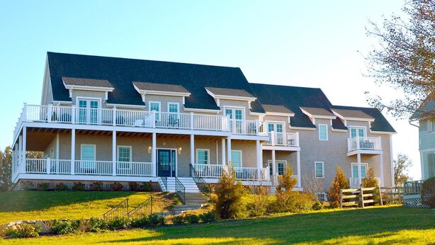 A multi-story building with a central entrance, balconies on each floor, and a well-maintained lawn in front. - The Inn at Spring House (Block Island)