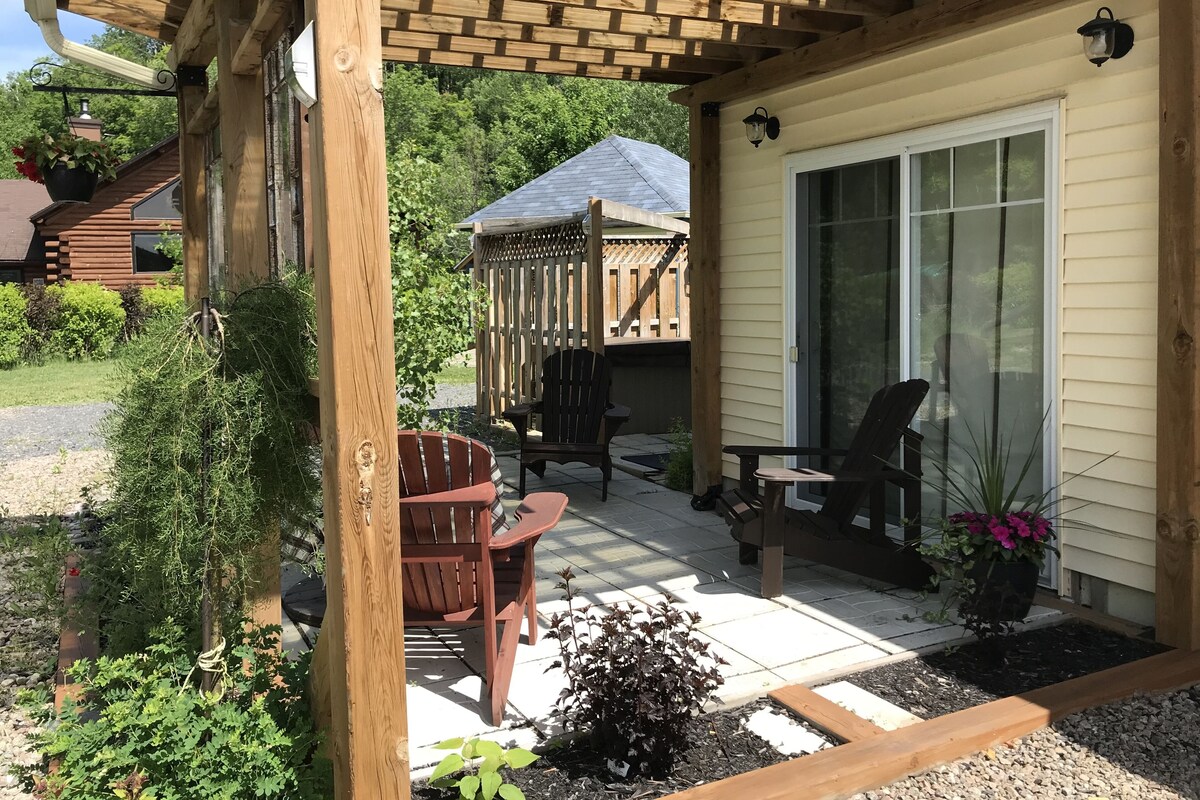 Eine überdachte Terrasse mit Holzmöbeln, ein kleiner Garten und ein Haus im Hintergrund.