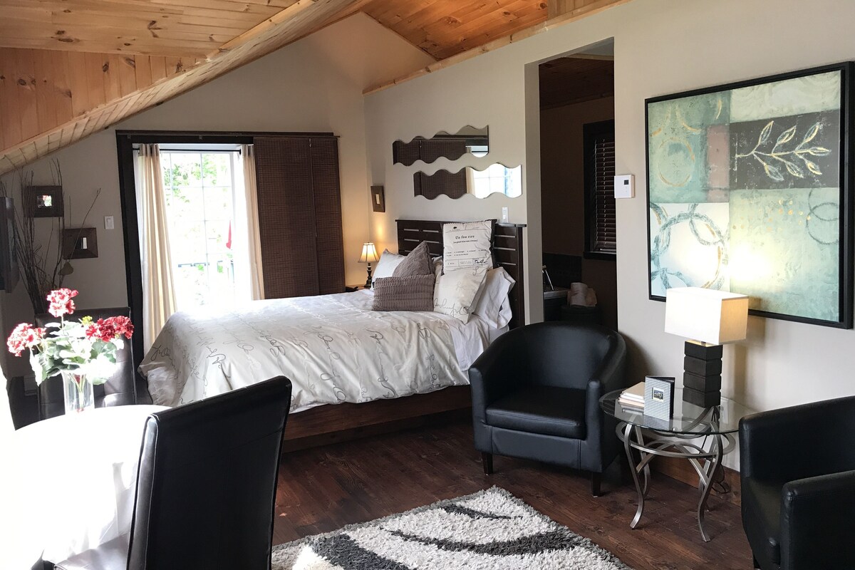 Ein Schlafzimmer mit Bett, Stuhl, Tisch und einem Gemälde.
