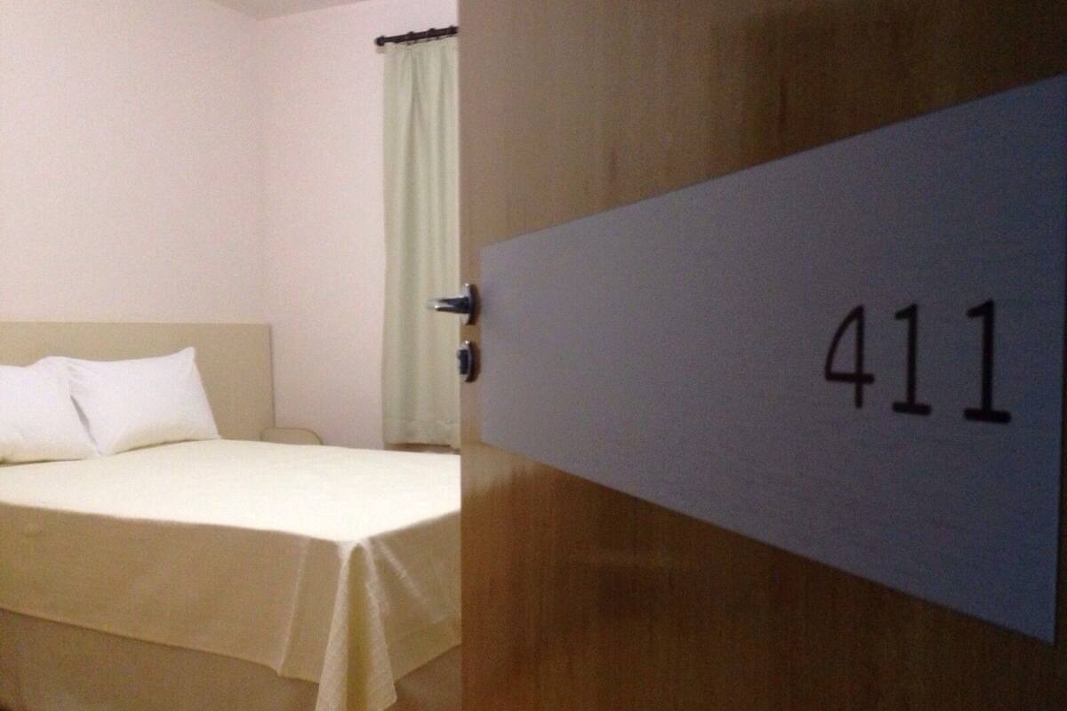 Una habitación de hotel con cama, una puerta con el número 411 y una cortina.