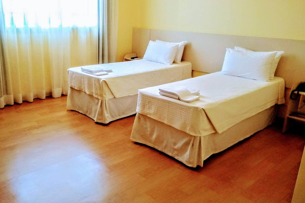 Habitación de hotel con dos camas, piso de madera y una ventana con cortinas.