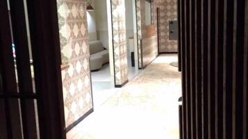 A corridor with patterned walls and a tiled floor, leading to a room with a bed and a desk.