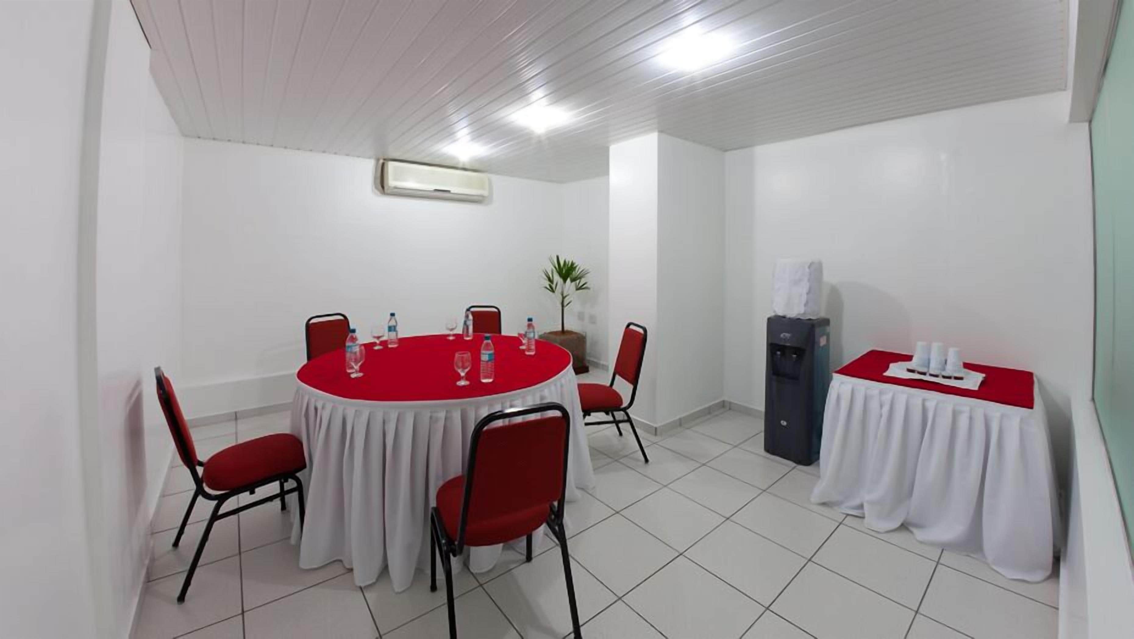 A conference room with a round table, red chairs, a water dispenser, and a small table with white tablecloths.