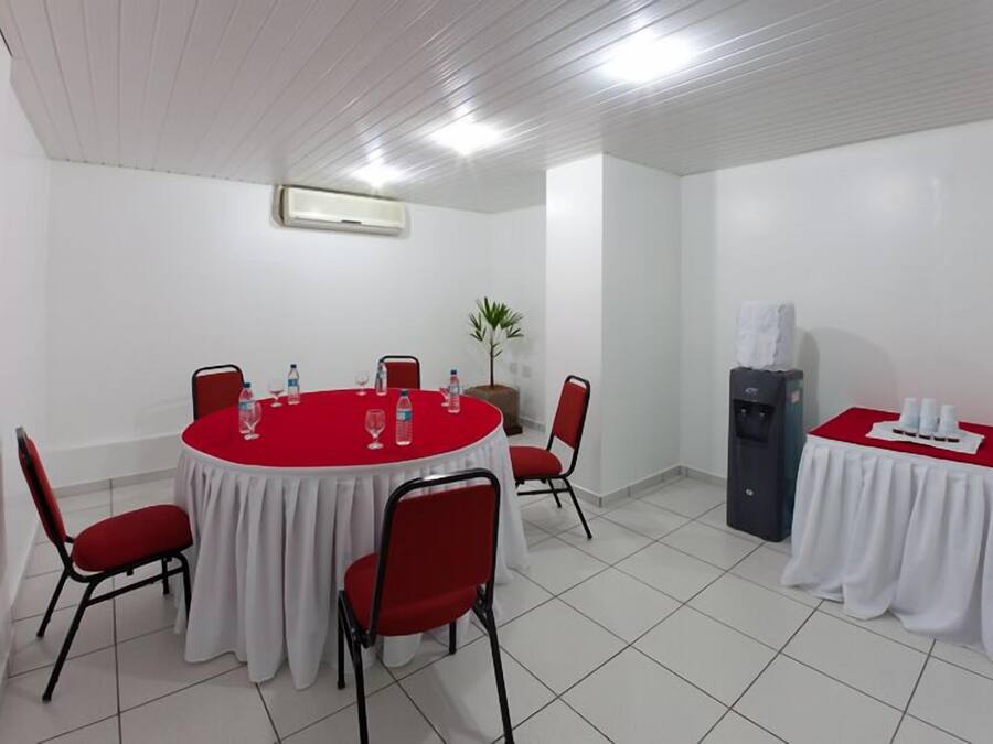 A conference room with a round table, red chairs, a water dispenser, and a small table with white tablecloths.