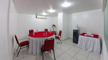 Una sala de conferencias con una mesa redonda, sillas rojas, un dispensador de agua y una pequeña mesa con mantel blanco.