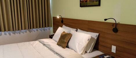 Une chambre d’hôtel avec un grand lit, une tête de lit en bois, deux tables de chevet et une petite table de nuit avec une lampe.