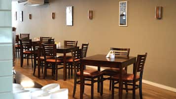 A dining area with wooden tables and chairs, a white tablecloth on one table, and framed pictures on the wall.