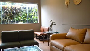 A living room with a sofa, a glass coffee table, and a view of a garden through a large window. - Belém Soft Hotel (Belém)