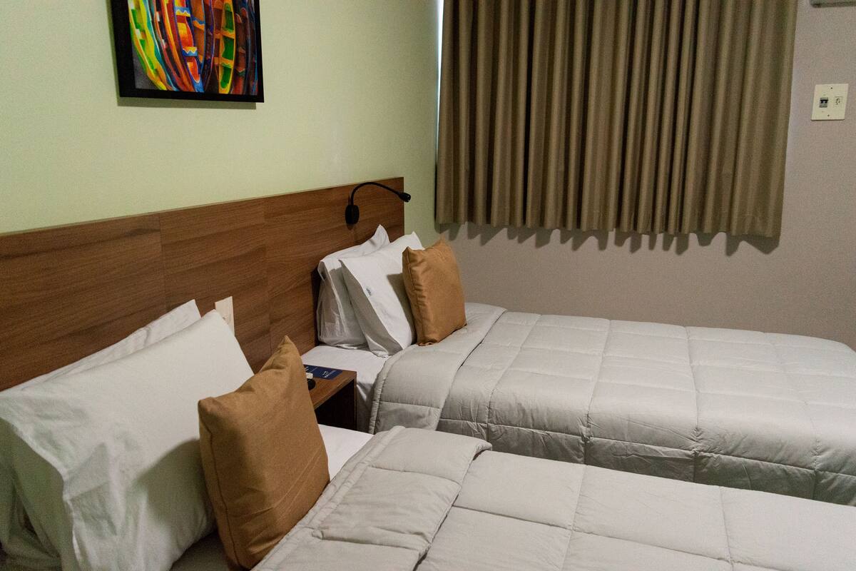 Ein Hotelzimmer mit zwei Betten, einem hölzernen Kopfteil, einem Bild an der Wand und einem Fenster mit Vorhängen.