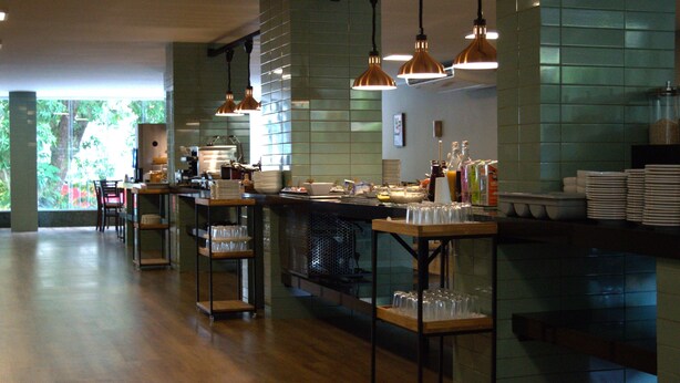A restaurant with a long counter, hanging pendant lights, and a view of greenery outside. - Belém Soft Hotel (Belém)