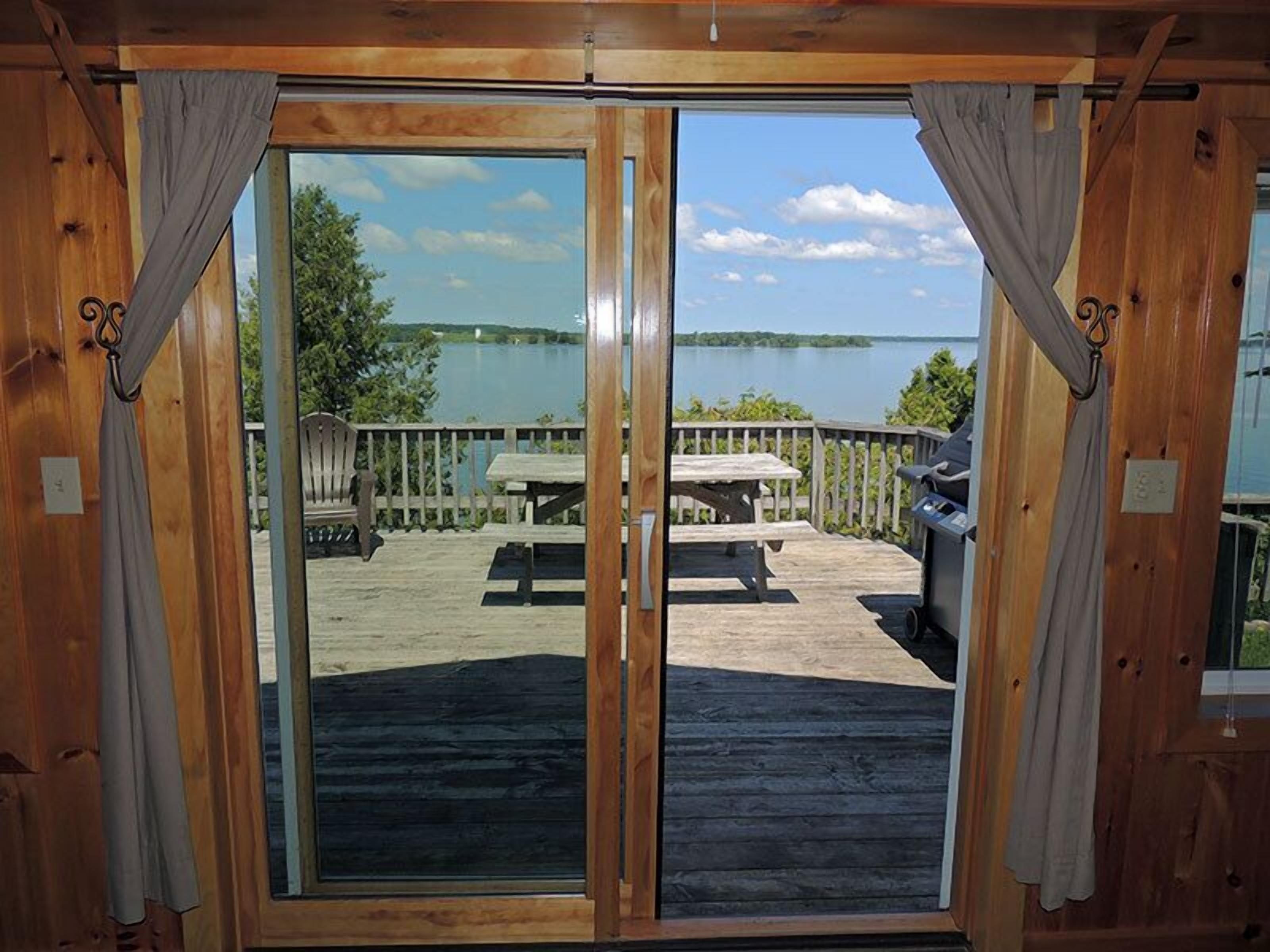 Une terrasse en bois avec une table de pique-nique et un barbecue, donnant sur un lac.