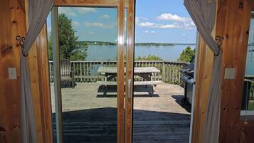 Una terraza de madera con mesa de picnic y parrilla, con vista a un lago.