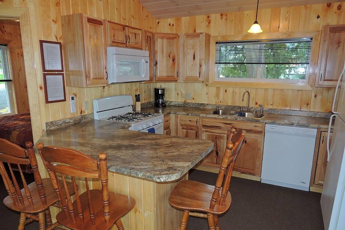 Una cocina de estilo rústico con isla central, sillas de madera, estufa, microondas y lavavajillas.
