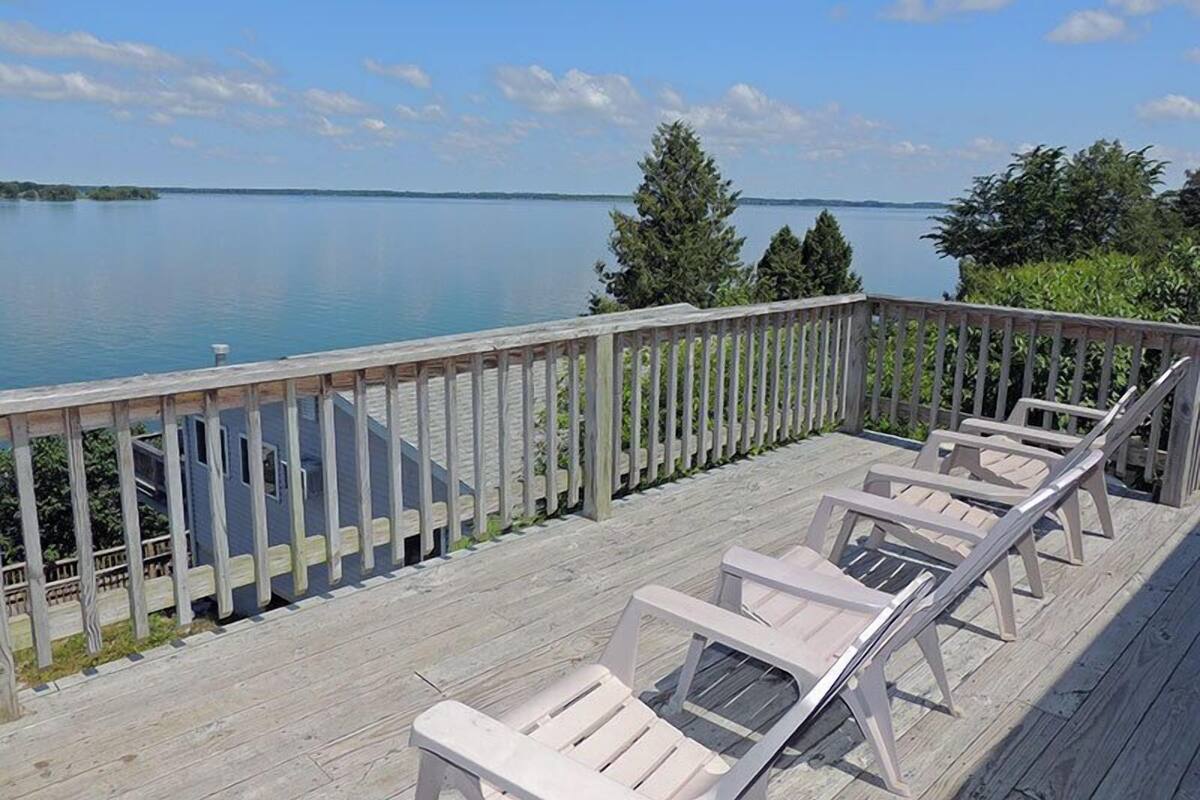 Una terraza con barandas de madera que da a un lago tranquilo, con varias sillas reclinables.