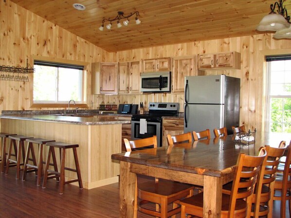 A wooden cabin-style kitchen with a central island, bar stools, and a dining table with chairs.