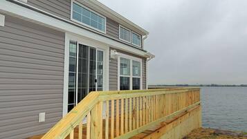 A two-story house with a wooden deck extending over a body of water.