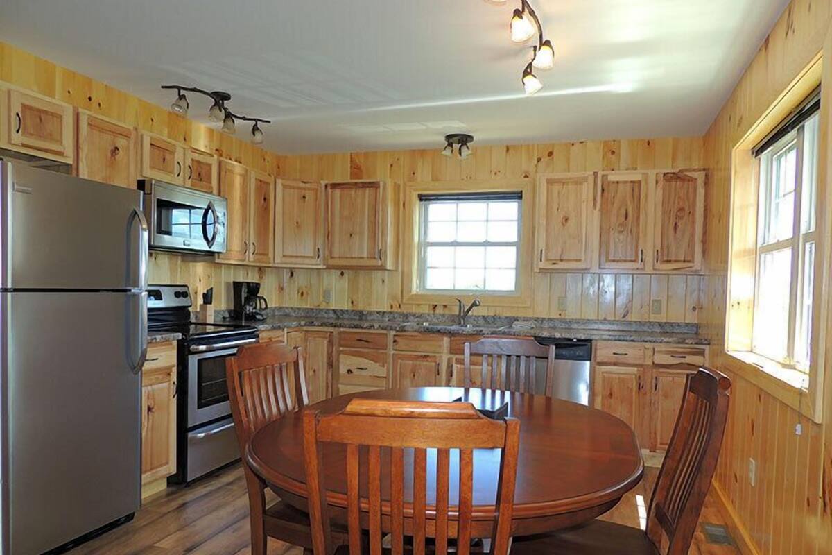 Una cocina con armarios de madera, un refrigerador de acero inoxidable, un microondas, un horno y una mesa de comedor con sillas.