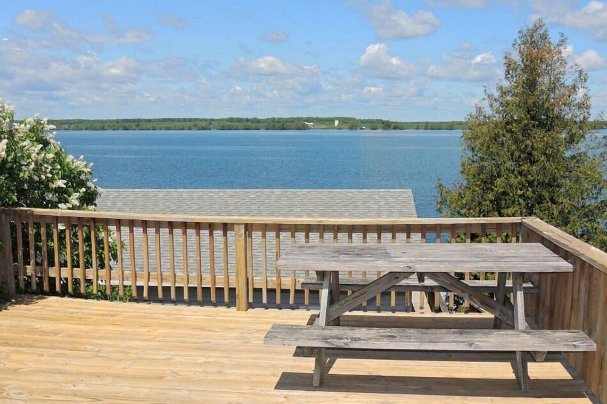 Una terraza de madera con mesa de picnic con vista a un lago.