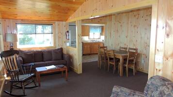 A wooden interior with a sofa, a rocking chair, a dining table with chairs, and a kitchen area.