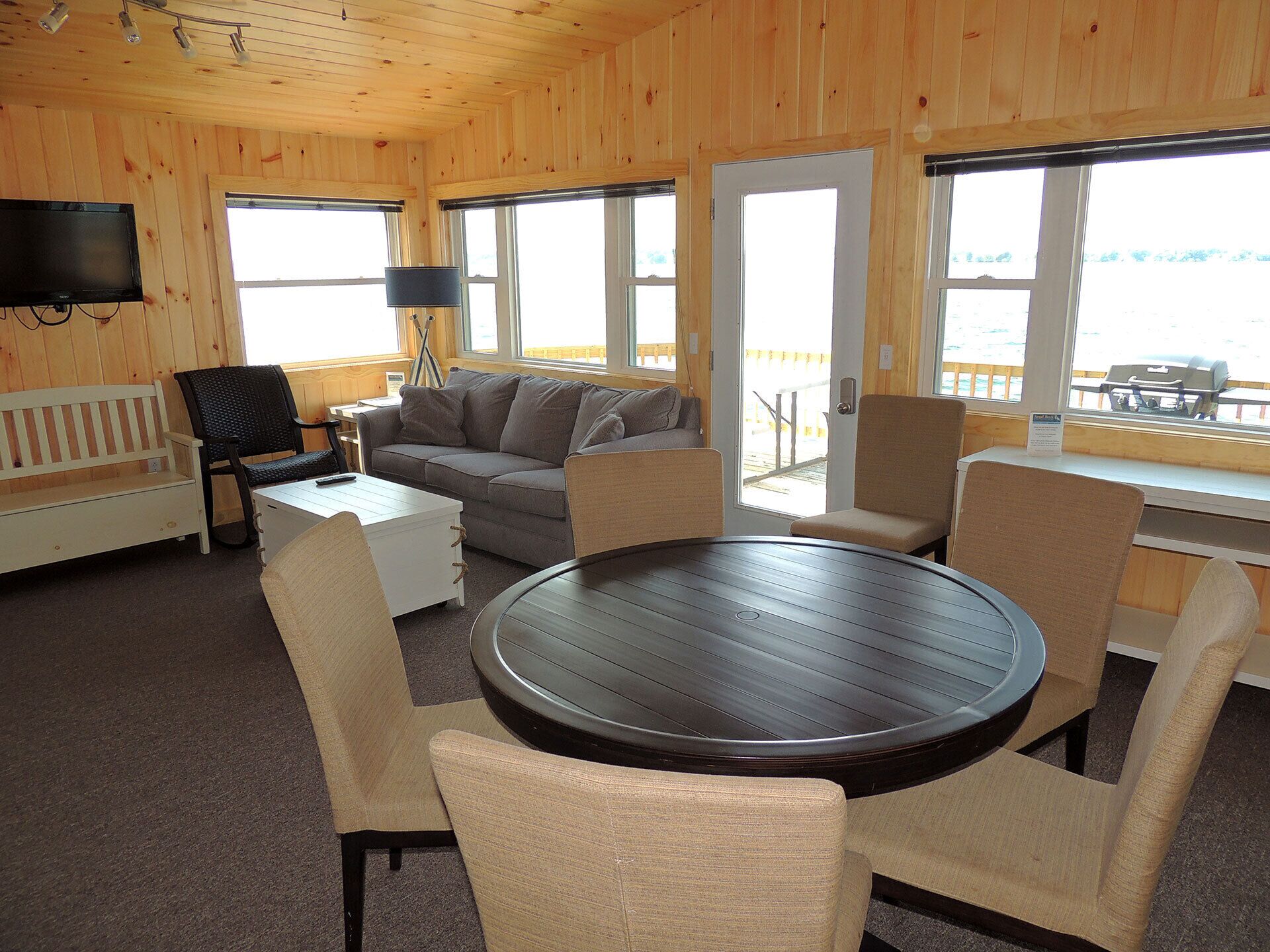 A cozy cabin interior with a sofa, chairs, a table, and a TV mounted on the wall.