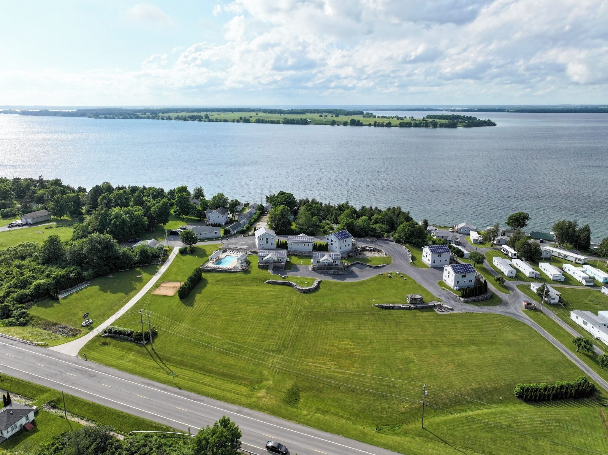 An aerial view of a lakeside residential area with houses, a swimming pool, and a road.