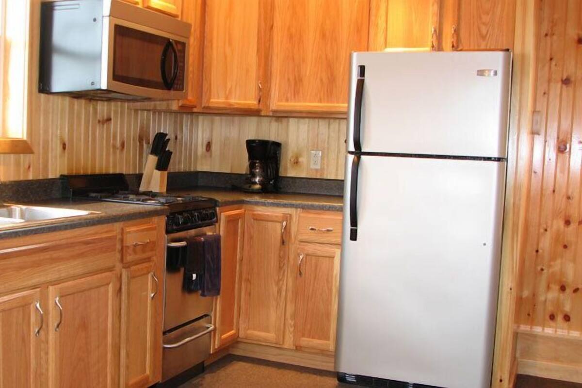 Una cocina con gabinetes de madera, un refrigerador de acero inoxidable, un microondas, una estufa y un lavaplatos.