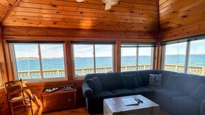 Un chalet confortable avec un intérieur en bois, un canapé, une petite table et de grandes fenêtres donnant sur un plan d’eau.