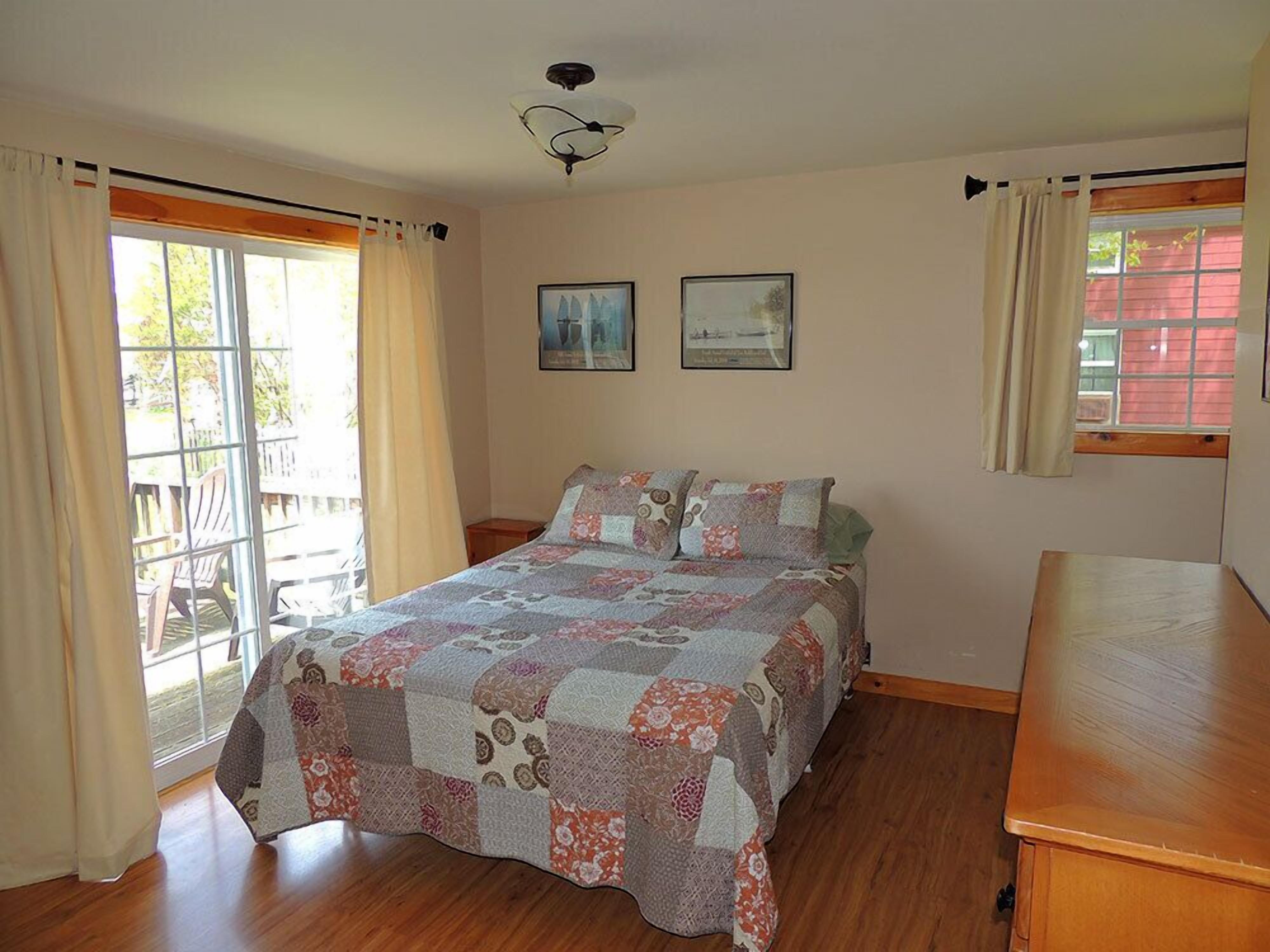 A bedroom with a wooden bed, a ceiling fan, two framed pictures, and a window with curtains.