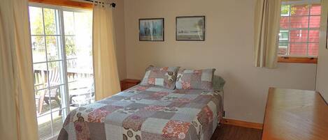 A bedroom with a wooden bed, a ceiling fan, two framed pictures, and a window with curtains.