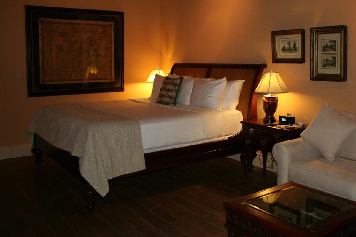 Une chambre d’hôtel avec un grand lit, une table de chevet avec une lampe, une chaise et des tableaux encadrés au mur.