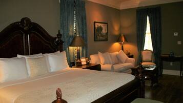 A hotel room with a large bed, a sofa, two lamps, a chair, and a small table.