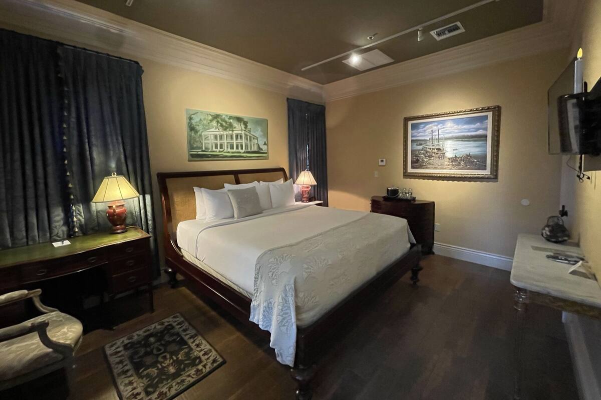 Une chambre à coucher avec un grand lit, une table de chevet, une lampe, une chaise, un tableau et un téléviseur.
