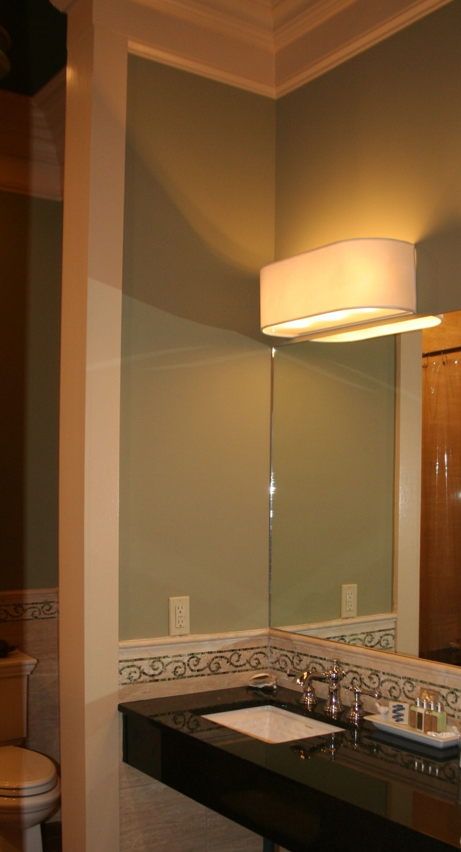 A bathroom with a large mirror, a sink with a black countertop, and a light fixture above the mirror.