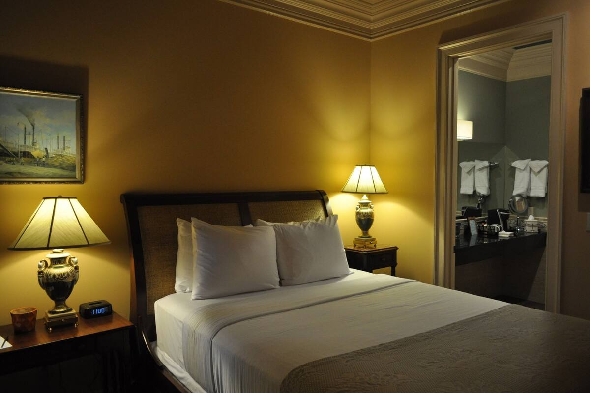 Une chambre d’hôtel avec un grand lit, deux lampes de chevet, une table de chevet avec une horloge et un tableau au mur.