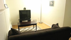 A living room with a dark sofa, a television on a stand, a coffee table, and a checkered rug. - Yellowknife Polar Suite (Yellowknife)