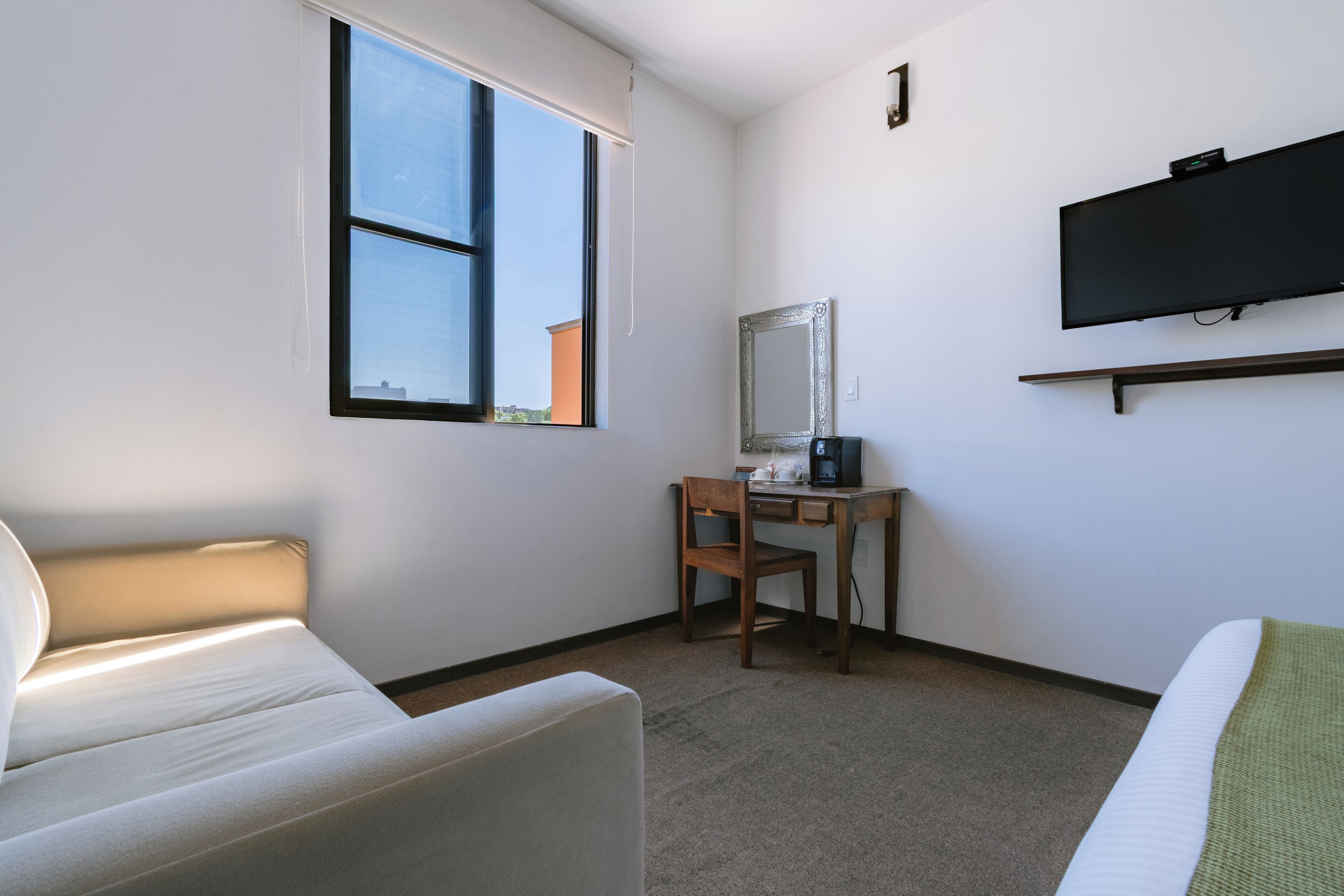 Habitación de hotel con cama, escritorio con silla, televisi ón montada en la pared y ventana con vistas al exterior.