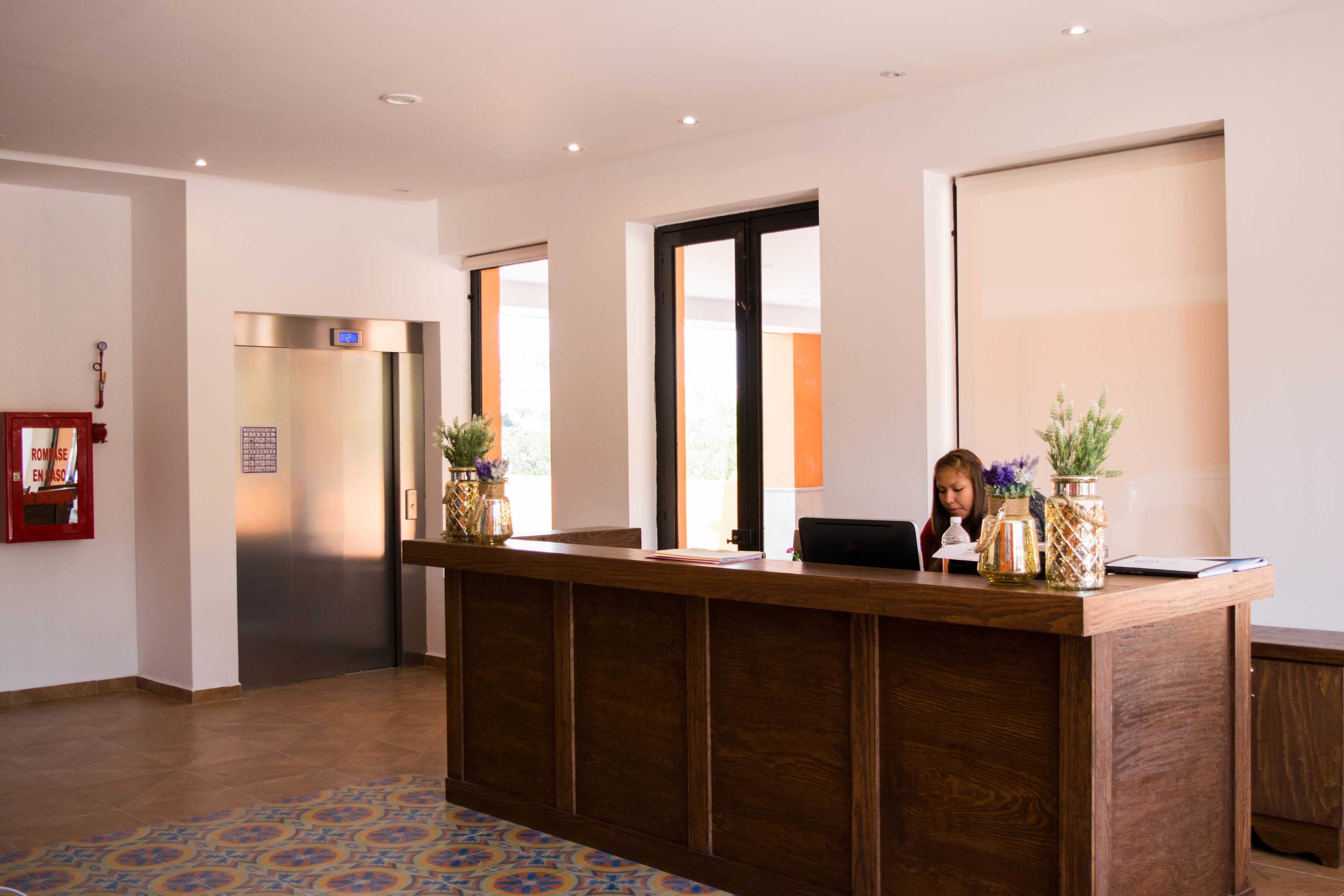 A reception desk with a wooden finish, a fire alarm, and a large window.