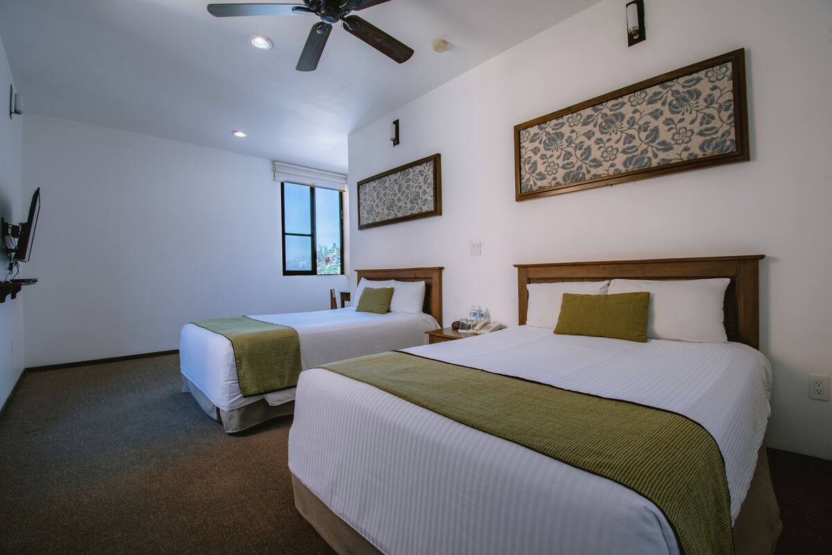 A hotel room with two beds, a ceiling fan, a window, and a floral wall decoration.