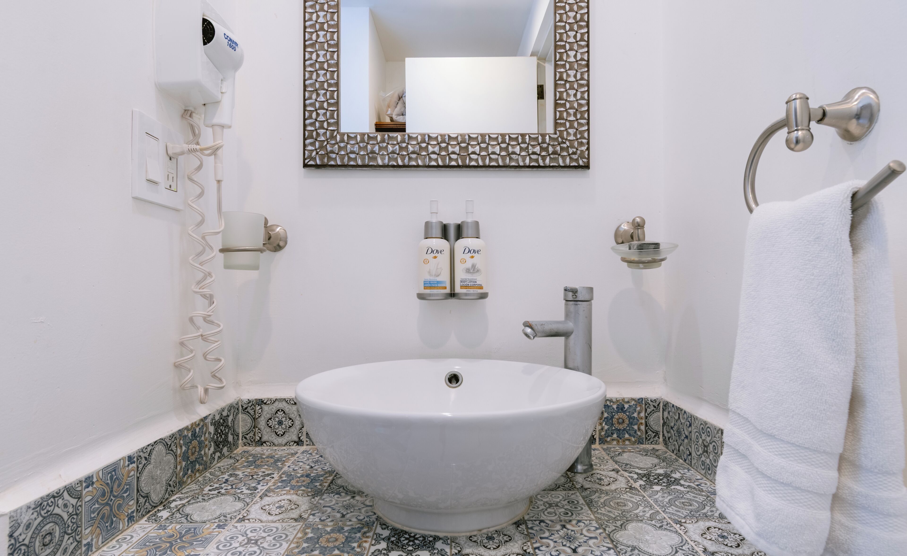 Un baño con lavamanos blanco, espejo, botellas de Dove y un perchero para toallas.
