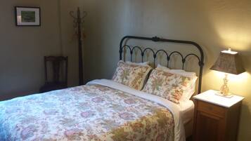 Een bed met bloemenbeddengoed, een bedlampje en een kapstok in een kamer met eenvoudige muren.