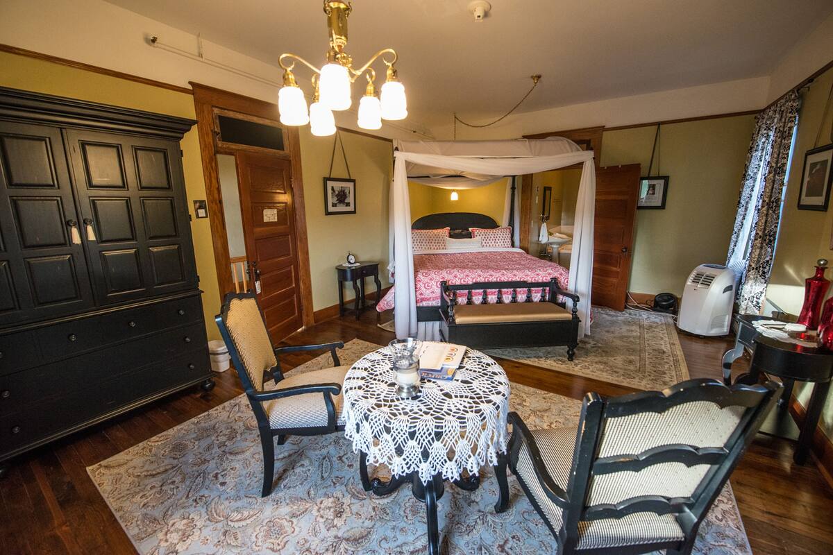 Un dormitorio con cama con dosel, candelabro, escritorio con silla y armario.