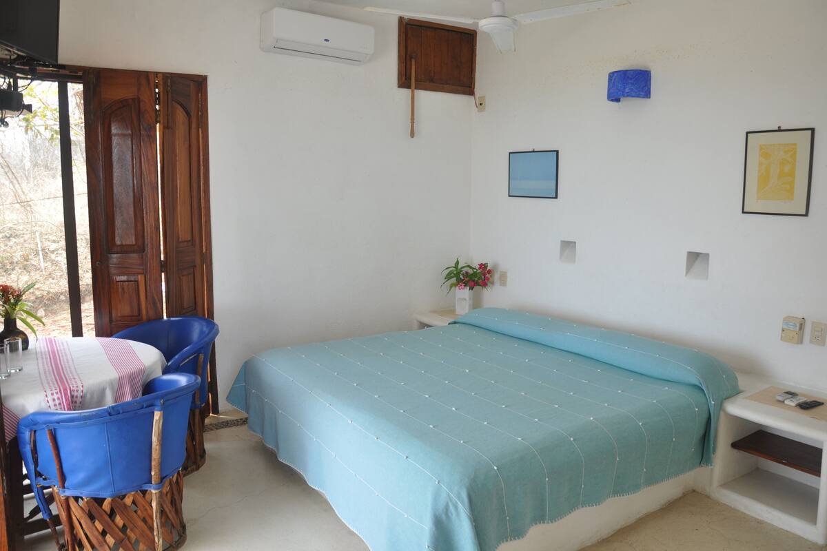 Een slaapkamer met een bed, een bureau met stoelen, een klein nachtkastje en een raam.