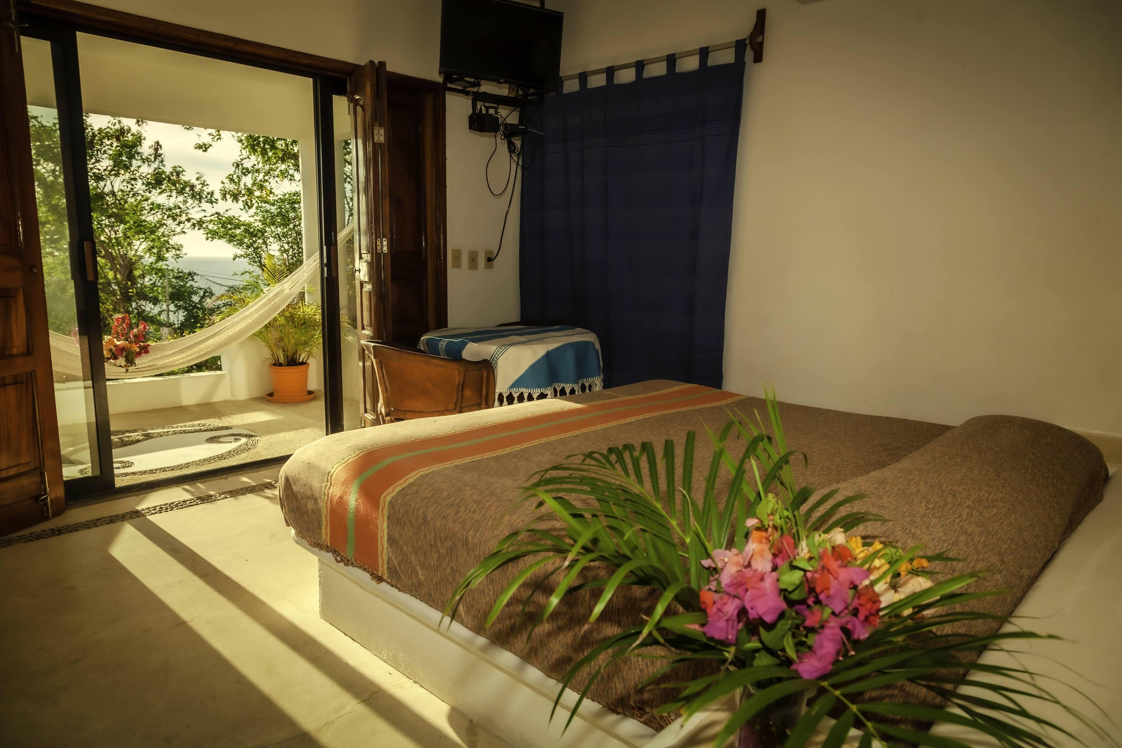 A bedroom with a bed, a hammock, and a view of the outdoors.