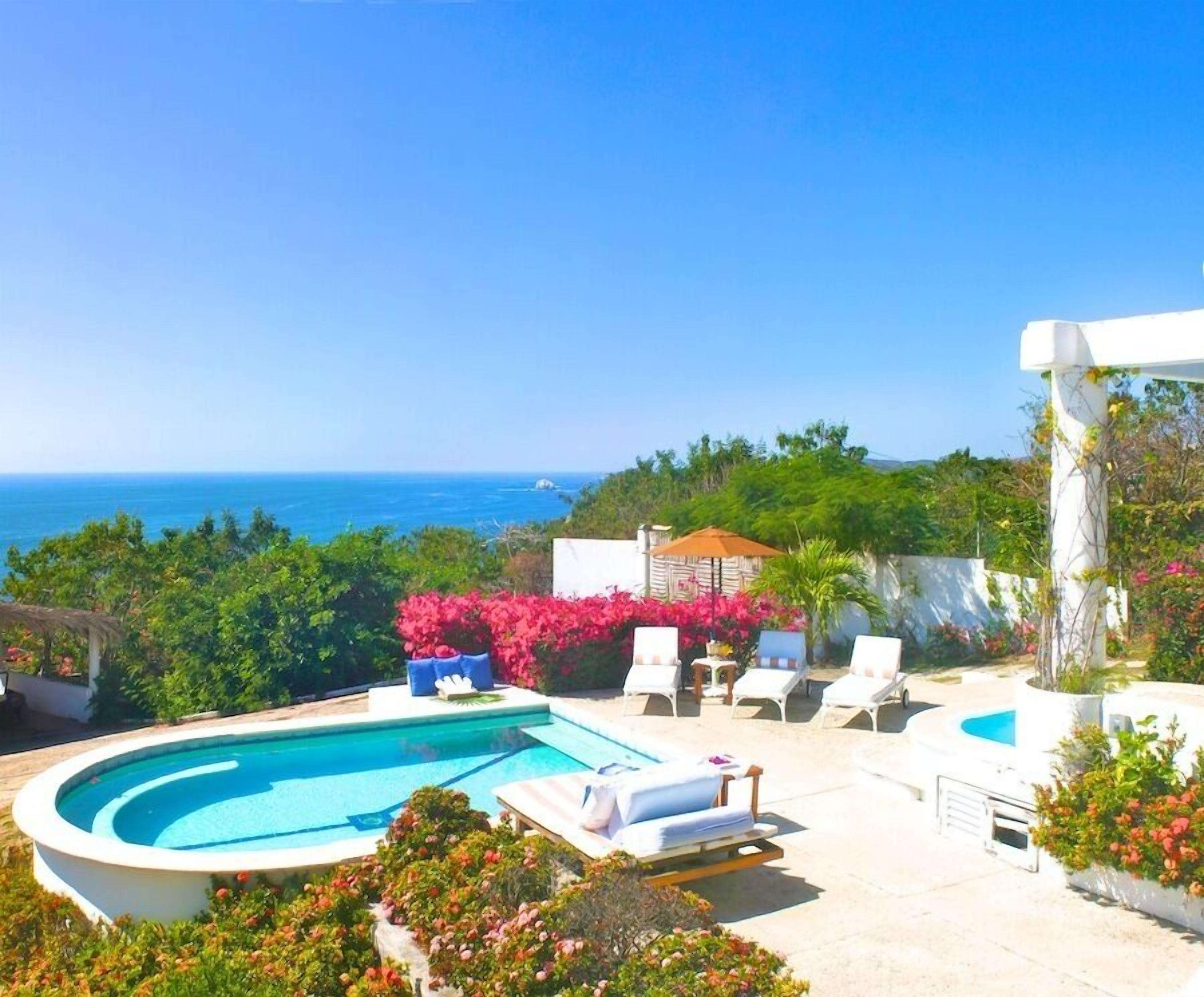 A pool area with lounge chairs and a view of the sea.